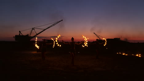 Fire-show-three-women-in-their-hands-twist-burning-spears-and-fans-in-the-sand-with-a-man-with-two-flamethrowers-in-slow-motion